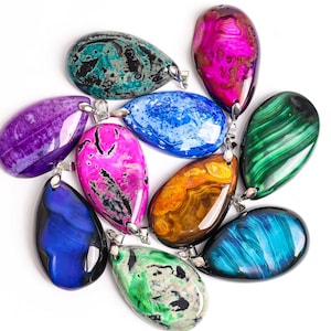Puede incluir: Colecci&oacute;n de colgantes de piedras preciosas en forma de l&aacute;grima en varios colores, incluyendo azul, verde, morado, rosa y naranja. Cada colgante tiene una argolla plateada para sujetar a una cadena. Las piedras tienen patrones &uacute;nicos.