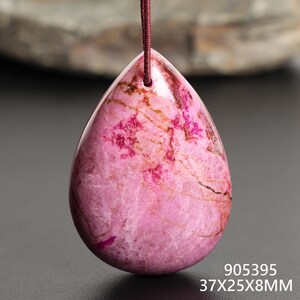 May include: A teardrop-shaped pink pendant with a brown cord. The pendant has a polished surface with darker pink and brown veining. The dimensions are 37x25x8mm.