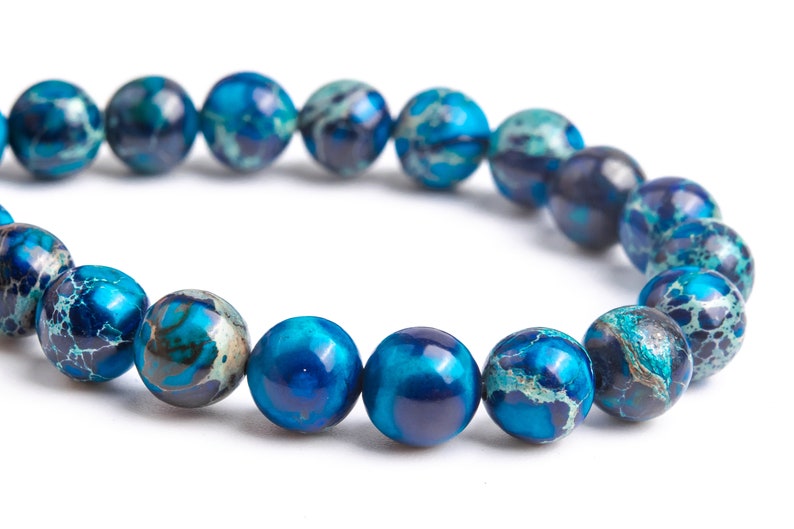 K&ouml;nnte beinhalten: Ein blaues und wei&szlig; gemustertes Perlenarmband. Die Perlen sind rund und haben eine marmorierte Optik.