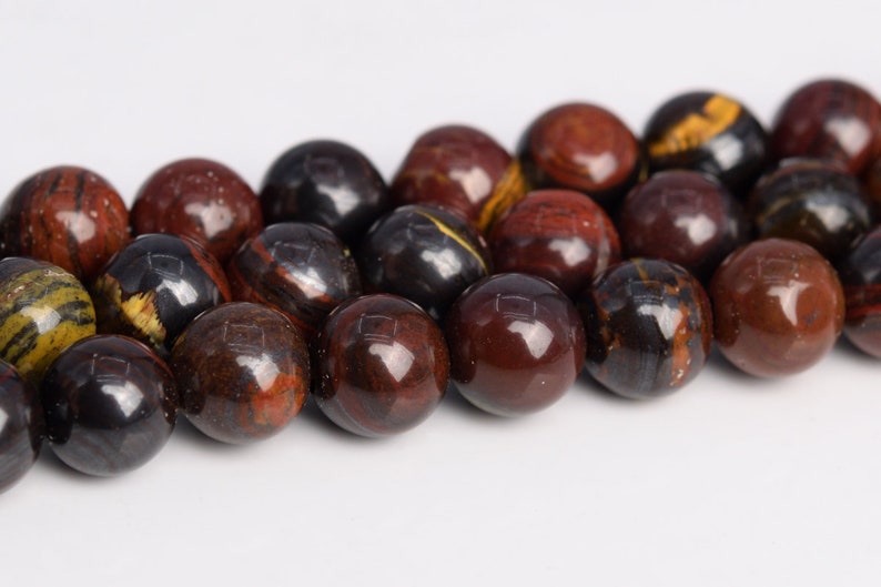 May include: A strand of round, red, black, and gold gemstone beads. The beads are polished and have a smooth, shiny finish.