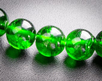Puede incluir: Primer plano de una hebra de cuentas de piedras preciosas verdes. Las cuentas son redondas y tienen un acabado liso y pulido. Las cuentas están enhebradas en un hilo transparente.