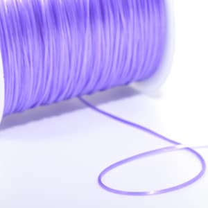 May include: A spool of lavender elastic cord, wound around a white plastic spool. The cord is unwinding from the spool, forming a loop.
