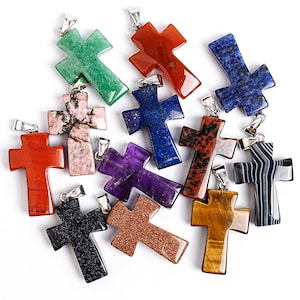 May include: A collection of gemstone cross pendants in various colors, including green, red, blue, purple, and black. Each cross has a silver-colored bail for attaching to a chain. The gemstones have unique patterns and textures.
