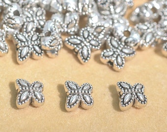May include: Silver butterfly shaped beads with a detailed design. The beads are small and have a hole in the center for stringing.