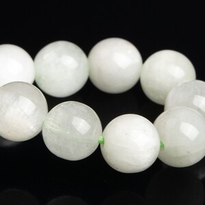 May include: A strand of white gemstone beads with a light green thread running through the center of each bead.