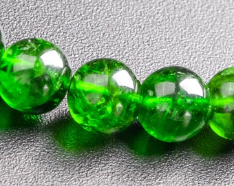 Puede incluir: Un primer plano de un brazalete de piedras preciosas verdes. El brazalete está hecho de cuentas redondas y pulidas que están enhebradas en un cordón elástico transparente.