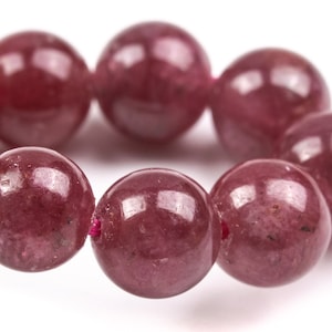 May include: A strand of round, red gemstone beads. The beads are smooth and polished, with a slight sheen.