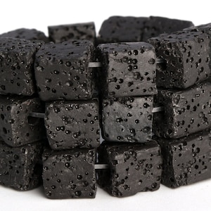 Puede incluir: Una hebra de cuentas de roca volcánica negra, cada cuenta es de forma cuadrada con una textura rugosa y porosa.