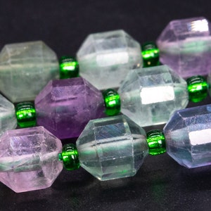 May include: A close-up of a multi-colored gemstone necklace. The necklace is made of faceted, octagonal beads in shades of green, purple, and blue. The beads are separated by small, green spacer beads.