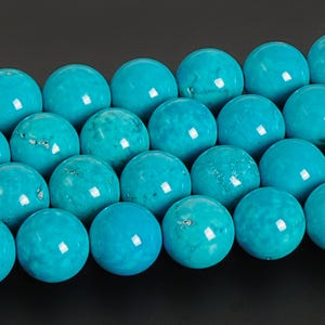 May include: Close-up of a strand of turquoise beads. The beads are a vibrant, solid turquoise color, with a smooth, polished surface. The beads are round and evenly sized, suggesting they are for jewelry making.