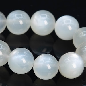 May include: A strand of white moonstone beads, each bead is round and smooth. The beads are strung together on a clear elastic cord.