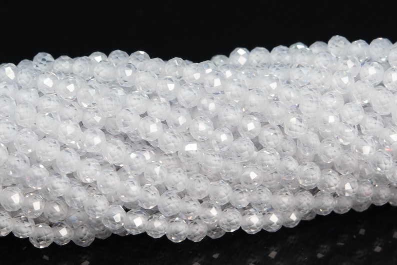 May include: A strand of white faceted gemstone beads. The beads are round and have a smooth, polished finish.