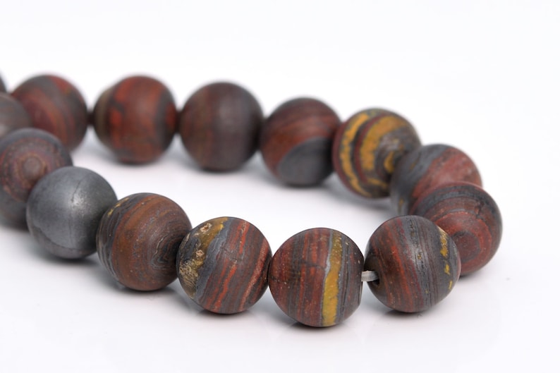 May include: A strand of round, red, brown, and gold striped beads. The beads are made of a natural stone with a layered pattern.