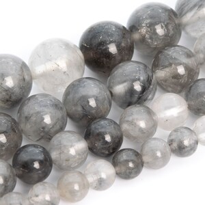May include: A strand of round, gray and clear gemstone beads. The beads have a translucent, cloudy appearance with black inclusions.