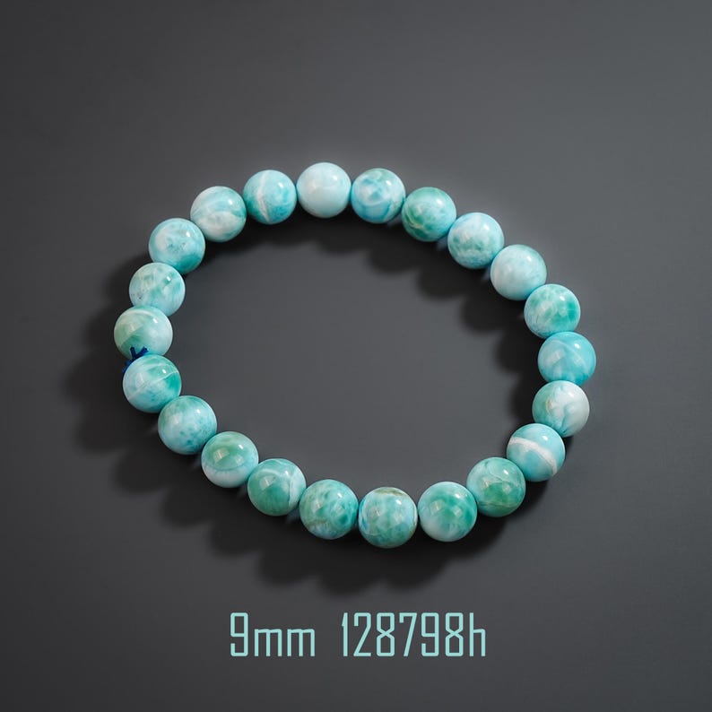 May include: A circular bracelet composed of round, polished 9mm beads in shades of light blue, turquoise, and white with marbled patterns. The beads are strung together in a continuous loop. The text 9mm 128798h is visible below the bracelet.