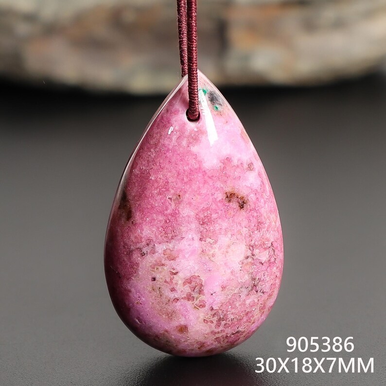 May include: A pink teardrop-shaped pendant with a maroon cord. The pendant is a polished stone with dark brown and white inclusions. The dimensions are 30x18x7mm.