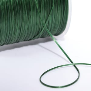 May include: A spool of dark green elastic cord, with a length of cord extending from the spool.