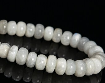 May include: A strand of polished, barrel-shaped moonstone beads. The beads are a milky white color with subtle variations and a soft sheen. The beads are strung together, creating a curved line against a black background.