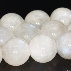 May include: A strand of white moonstone beads, each bead is a smooth, round sphere. The beads are arranged in a line, with the light reflecting off their surfaces.