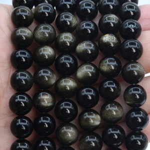 May include: A strand of black and gold gemstone beads. The beads are round and have a smooth, polished finish. The beads are strung on a clear elastic cord.