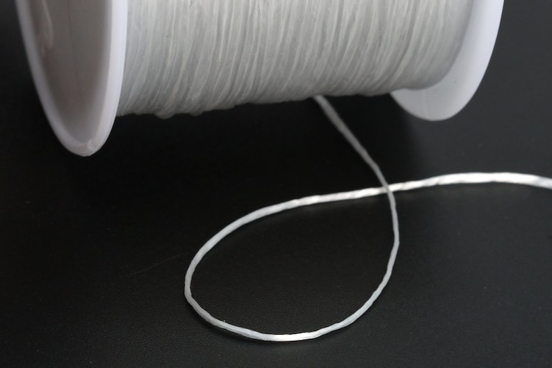 May include: A spool of white elastic cord, with a length of cord extending from the spool.