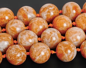 May include: Close-up of a necklace featuring large, round beads. The beads are a warm orange color with white marbling, strung together with orange thread. The beads have a polished, glossy finish, and the background is black.