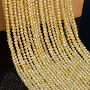 Puede incluir: Primer plano de m&uacute;ltiples hebras de cuentas facetadas de color amarillo dorado. Las cuentas son peque&ntilde;as y redondas, con una superficie brillante y reflectante. Las hebras est&aacute;n dispuestas muy juntas, creando una apariencia densa y texturizada. El fondo es oscuro.