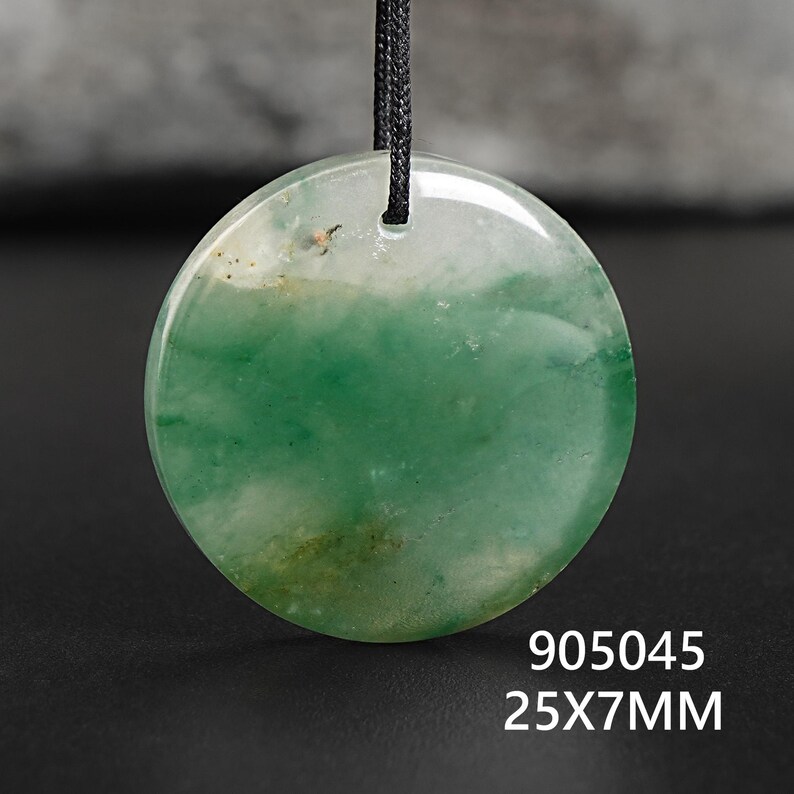 Pu&ograve; includere: Ciondolo rotondo in giada verde e bianca, con cordino nero. La pietra lucida misura 25 mm x 7 mm. Il ciondolo ha un aspetto naturale e traslucido.