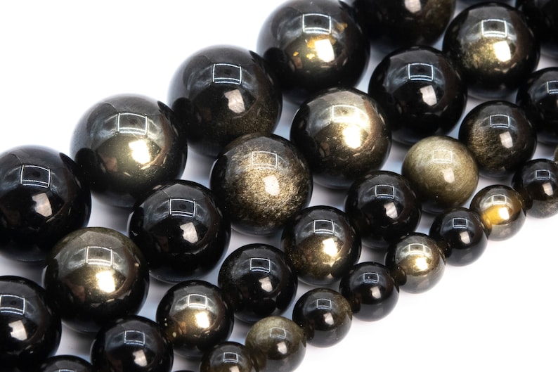May include: A strand of black obsidian beads with gold flecks. The beads are round and smooth, and they are strung on a clear elastic cord.