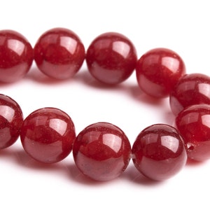 Puede incluir: Una hebra de cuentas de piedras preciosas de color rojo intenso, cada cuenta es redonda y lisa, con un acabado brillante.