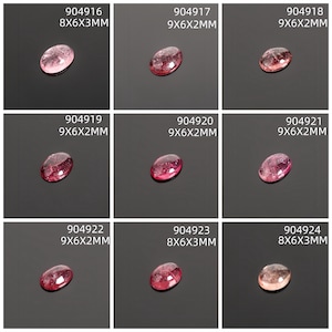 May include: Nine oval-shaped gemstones in shades of pink and red are displayed against a dark background. Each gem has a unique color variation and is labeled with a product code and dimensions in millimeters. The gemstones are likely for jewelry making.
