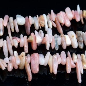 Puede incluir: Una hebra de cuentas de piedras preciosas rosadas y blancas, con una variedad de formas y tamaños. Las cuentas están enhebradas en un hilo transparente y están dispuestas en un patrón aleatorio.
