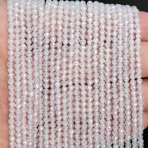 May include: A strand of white faceted crystal beads. The beads are small and round, and they have a shiny, reflective surface.