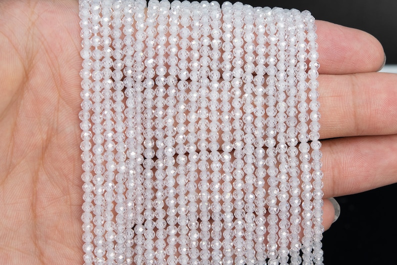 May include: A strand of white faceted crystal beads. The beads are small and round, and they have a shiny, reflective surface.