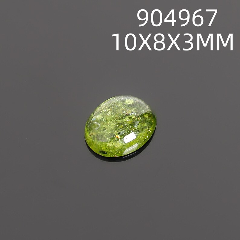 May include: A translucent, oval-shaped gemstone with a vibrant green hue. The gem measures approximately 0.4 x 0.3 x 0.1 inches and features inclusions within its structure. The text "904967 10X8X3MM" is displayed above the gem.