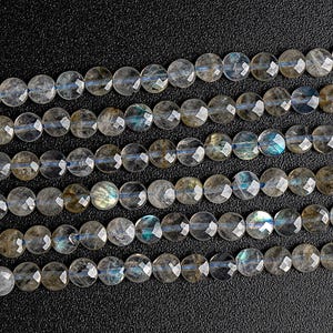 May include: A strand of round, faceted labradorite beads in shades of gray and blue. The beads are strung on a clear thread and have a natural, iridescent sheen.