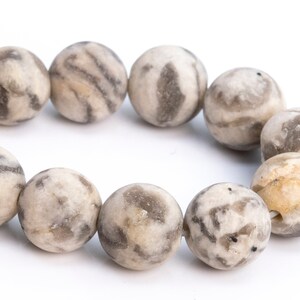 May include: A strand of round, gray and white agate beads with a marbled pattern. The beads are strung together on a clear string.