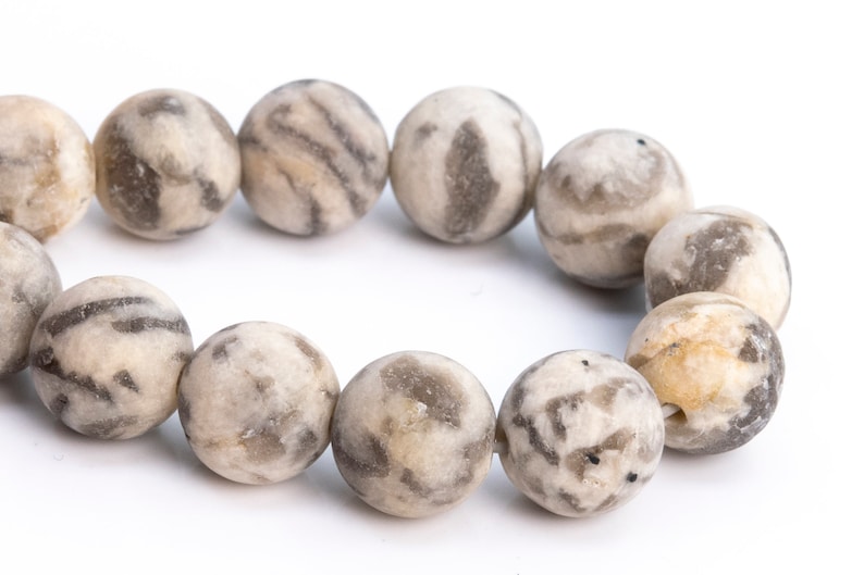 May include: A strand of round, gray and white agate beads with a marbled pattern. The beads are strung together on a clear string.