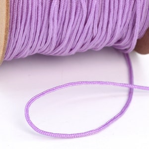 May include: A spool of light purple waxed cord, with a length of cord extending from the spool.