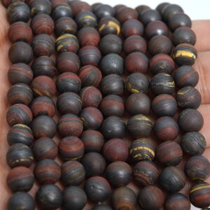 May include: A strand of round, dark brown, red, and gold striped beads. The beads are made of natural stone and have a smooth, polished finish.