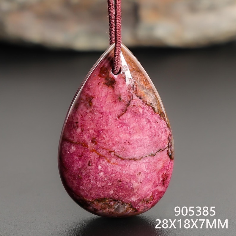 May include: A teardrop-shaped pendant with a pink and brown marbled pattern. The pendant is suspended from a maroon cord. The dimensions are 28x18x7mm.