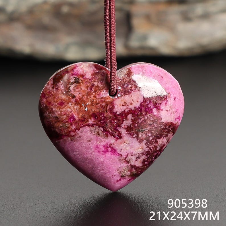 May include: A heart-shaped pendant with a pink and brown mottled pattern, suspended by a maroon cord. The pendant measures approximately 0.83 x 0.94 x 0.28 inches. The pendant has a glossy finish and is likely made of stone.