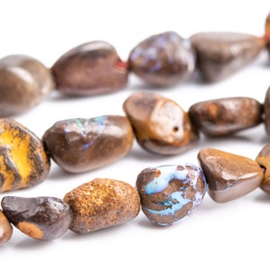 May include: Close-up of a strand of polished, tumbled gemstones in shades of brown, tan, and orange. Some stones have unique patterns and colors, including yellow and blue. The stones are strung together with a red string.
