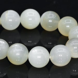 May include: A strand of white moonstone beads, each bead is round and smooth. The beads are strung together on a clear elastic cord.