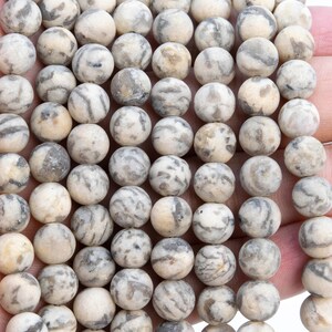 May include: A strand of round, white and gray agate beads. The beads have a natural, marbled pattern.