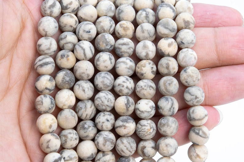 May include: A strand of round, white and gray agate beads. The beads have a natural, marbled pattern.