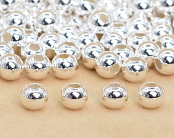 Può includere: Primo piano di un mucchio di perline di metallo color argento. Le perline sono rotonde e hanno un foro al centro. Le perline sono disposte in uno schema casuale.