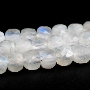 May include: A strand of white moonstone beads with a faceted, square shape. The beads have a subtle iridescent sheen.