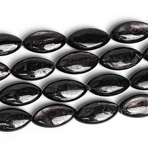 Pode incluir: Um fio de contas de pedras preciosas pretas de forma oval. As contas têm um acabamento brilhante e iridescente.