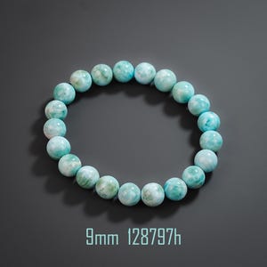 May include: A circular bracelet composed of smooth, round, light blue and white marbled beads. The beads measure 9mm in diameter as indicated by the text 9mm 128797h printed below the bracelet. The stones feature a polished finish.